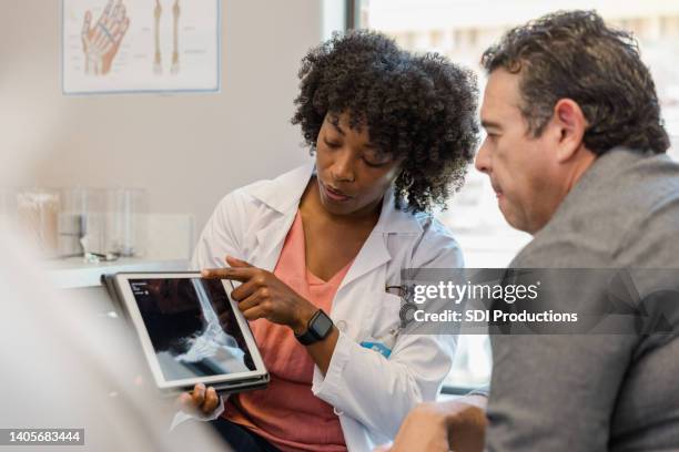 female orthopedic surgeon points to foot x-ray on digital tablet - röntgen stockfoto's en -beelden