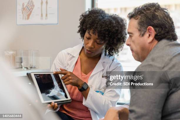 female orthopedic surgeon points to foot x-ray on digital tablet - orthopedic surgery stock pictures, royalty-free photos & images