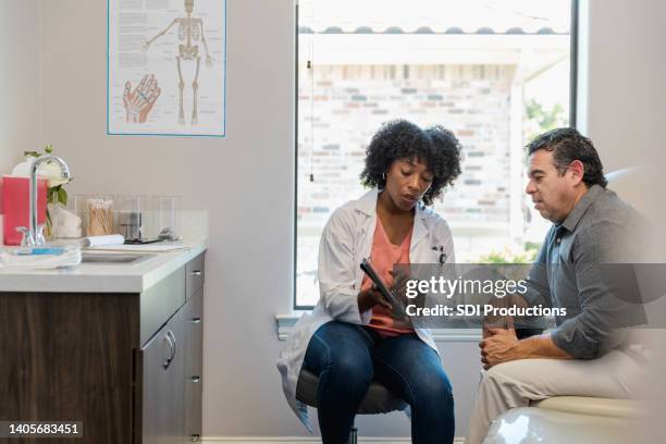 female doctor points to something on tablet as patient listens - doctor with patient man stockfoto's en -beelden