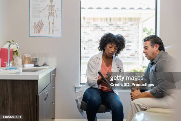 female doctor points to something on tablet as patient listens - mature adult with doctor stock pictures, royalty-free photos & images
