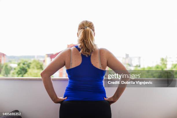 chubby woman doing warm up exercises on a balcony, rear view - obesity stock pictures, royalty-free photos & images