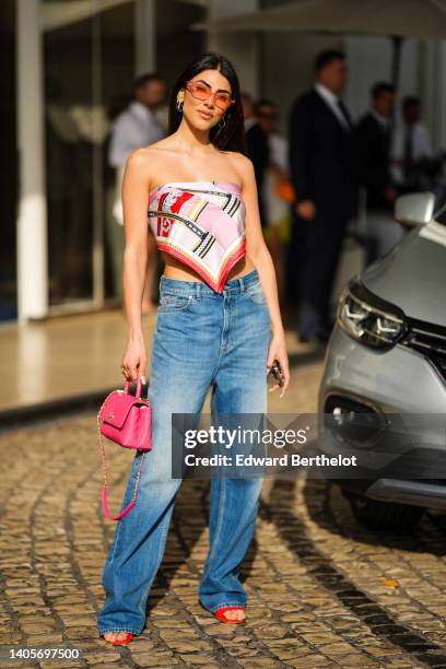 Giulia Salemi wears orange sunglasses, gold earrings, a pink / red / black / gold print pattern silk scarf as a shoulder-off top, a pink shiny...