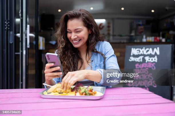 glückliche frau, die sich die sozialen medien ansieht, während sie tacos isst - mexican food stock-fotos und bilder