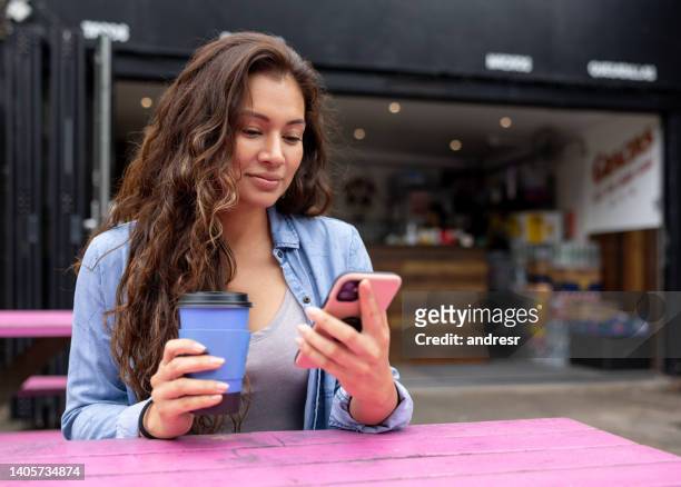 schöne frau, die eine tasse kaffee im freien trinkt, während sie ihr telefon benutzt - business forum in london stock-fotos und bilder