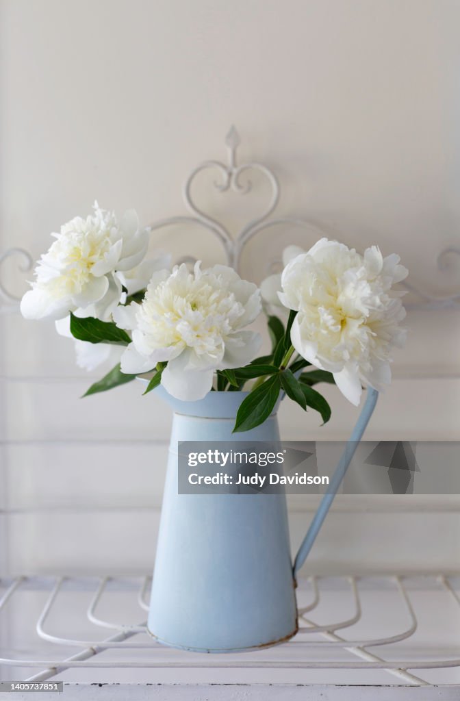 Vintage blue enamelware pitcher vase with white peonies on antique painted baker's rack