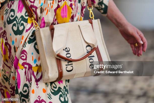 Guest wears a white with multicolored print pattern long dress, a white fabric with embroidered brown leather crossbody bag from Chloé, during the...