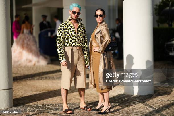 Alejandro Acero wears brown sunglasses, a white with black and yellow flower print pattern wool shirt, high waist beige suit pants, black shiny...