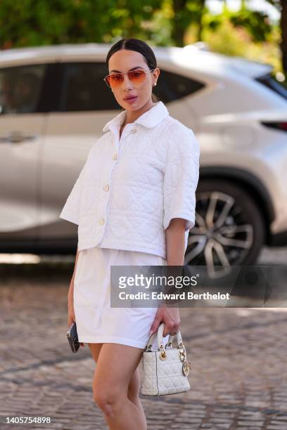 Sira Pevida wears orange sunglasses, pearl earrings, a white quilted pattern / buttoned short sleeves jacket from Dior, a white short dress, a white...