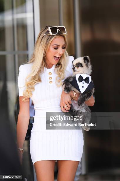 Guest wears beige square sunglasses, a diamond necklace, a white ribbed pattern / large gold buttons neck / short sleeves / short tube dress, a gold...