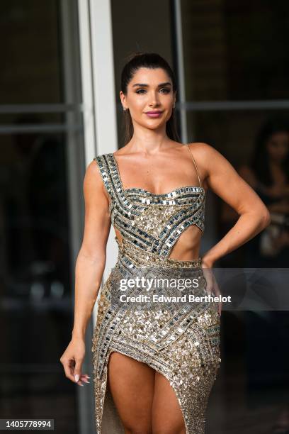 Guest wears a silver and gold embroidered mirror and sequined asymmetric tank-top / cut-out waist / slit long dress , during the 75th annual Cannes...