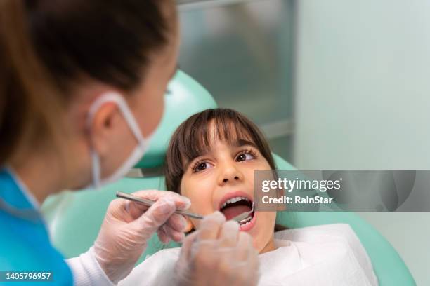dentista en el consultorio del dentista examinando los dientes de la niña - odontopediatría fotografías e imágenes de stock