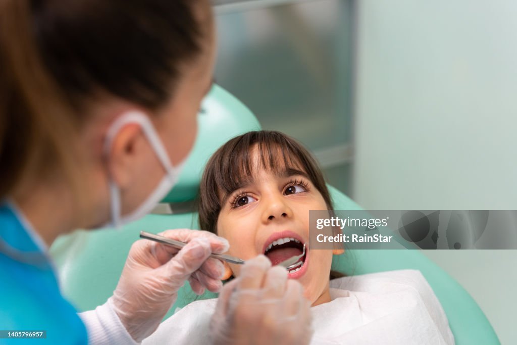 Dentista no consultório do dentista examinando os dentes da menina