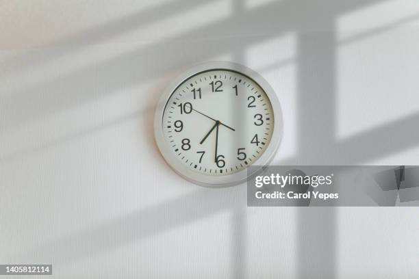 a simple white wall clock above a sunny window, in the afternoon - clock on wall stock pictures, royalty-free photos & images