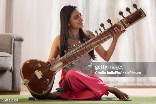 portrait of young female musician playing sitar at home - sitar photos et images de collection