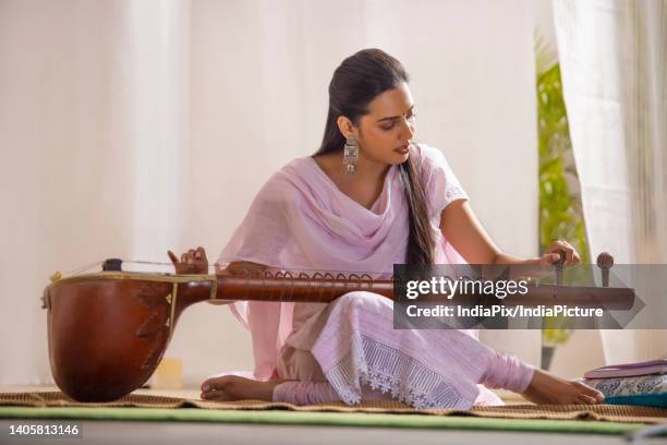 young female musician tuning her sitar while sitting in living room - sittar stock pictures, royalty-free photos & images