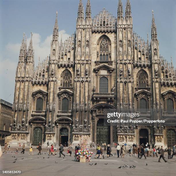 Pedestrians walk across Piazza del Duomo in front of the main western entrance to Milan Cathedral in the city of Milan in the Lombardy region of...