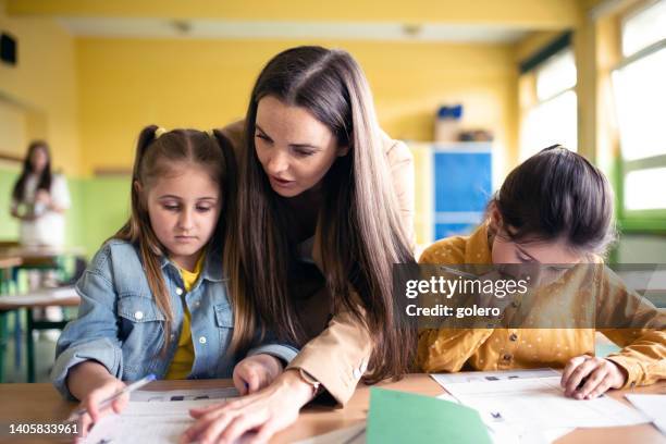 young female teacher explaining to school girls at desk in lesson - workbook stock pictures, royalty-free photos & images
