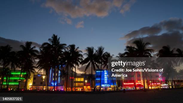 Art Deco District, Miami Beach shows colorful retro neon signs with palm trees and clouds on beach, Florida.