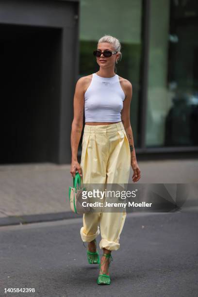 Nina Sieber seen wearing brown Celine Triomphe sunglasses, gold earrings, a white crop top from NØNOUC studios, a yellow oversized pants from Maison...