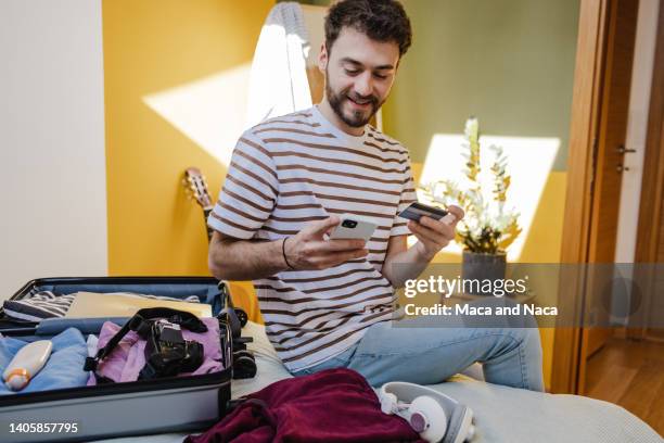 young man buying tickets online and preparing for a trip - booking hotel stock pictures, royalty-free photos & images