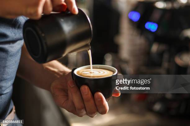 close up shot of barista pouring milk in a cup with coffee, creating latte art - barista coffee milk stock pictures, royalty-free photos & images