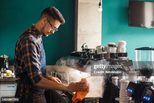 barista mit einem dampfgarer auf einer espressomaschine bei der vorbereitung von kundenbestellungen - kaffeemaschine stock-fotos und bilder