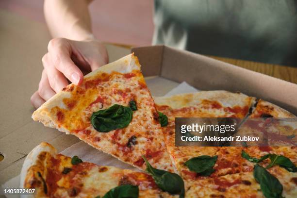 a beautiful stylish woman in sunglasses takes a piece of vegetarian pizza to eat it. italian cuisine in a pizzeria. sliced pizza in a paper delivery box, on a wooden table in a pizzeria. delicious lunch, snack, fast food. - pizza crust stock pictures, royalty-free photos & images