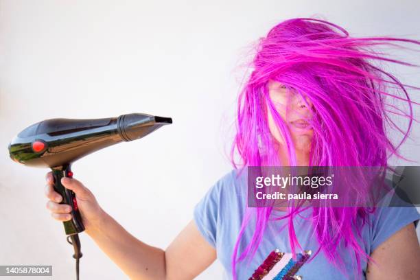 woman wearing pink wig using hair dryer - drying hair stock-fotos und bilder