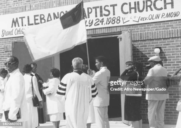 Wide shot of clergy and parishioners, one holding a flag, congregating near the entrance to the newly built Mount Lebanon Baptist Church in...
