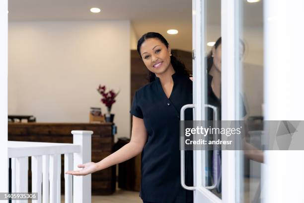 happy esthetician welcoming clients to a spa at the door - beautician client stock pictures, royalty-free photos & images