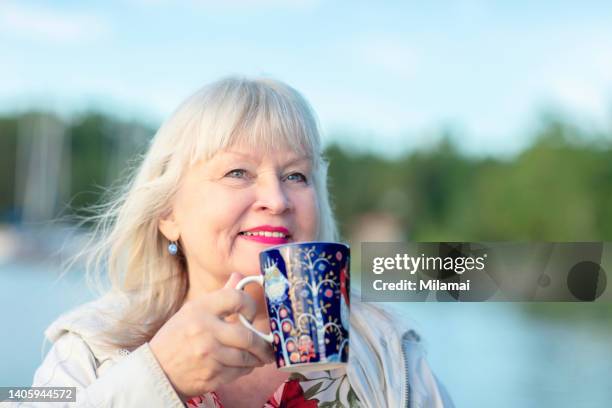 beautiful senior woman drinking coffee near lake at summer - turku bildbanksfoton och bilder