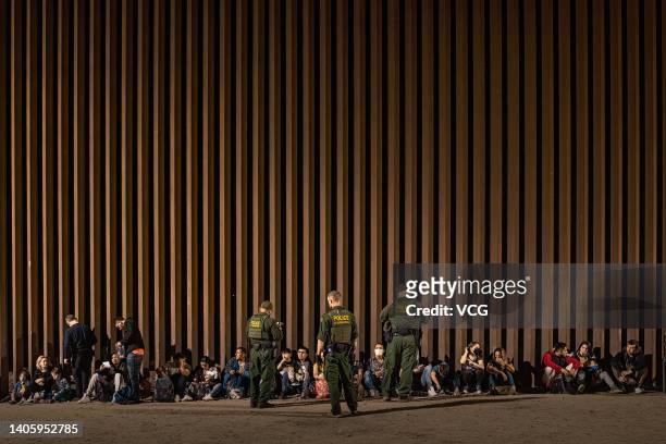 Border Patrol agents keep watch as immigrants wait to be processed by the U.S. Border Patrol after crossing the border from Mexico, with the...