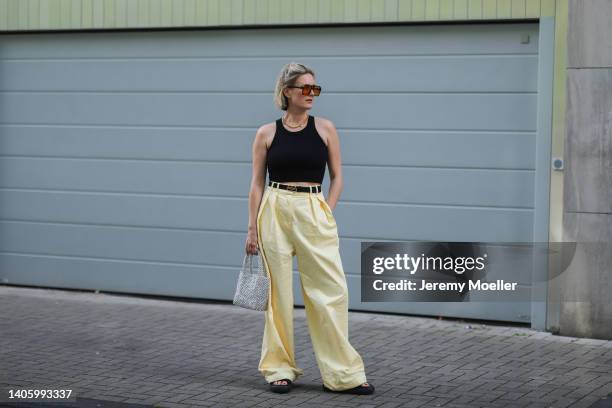 Victoria Thomas seen wearing a brown sunglasses with yellow lenses from Lamarel, a gold necklace, gold earrings, a black crop top, a yellow wide leg...