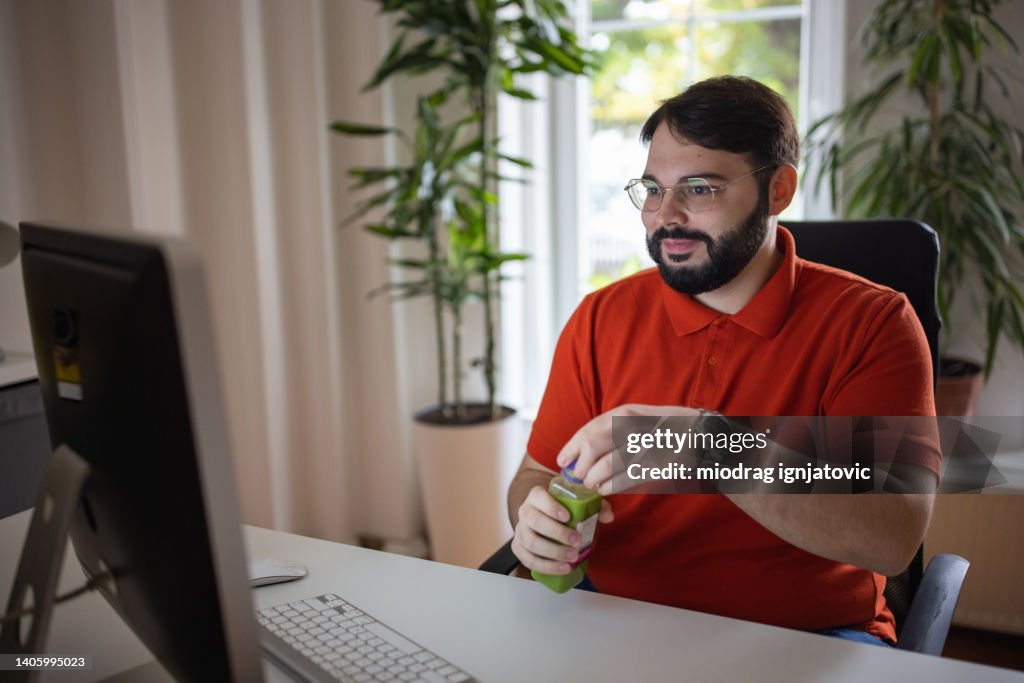 Caucasian man working from the modern office while drinking green smoothie