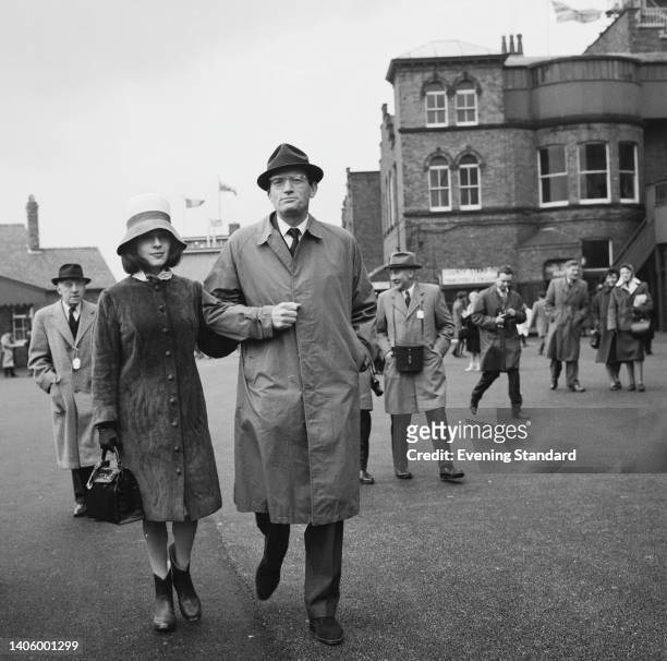 French-American journalist and arts patron Veronique Peck arm-in-arm with her husband, American actor Gregory Peck attend the 1963 Grand National,...