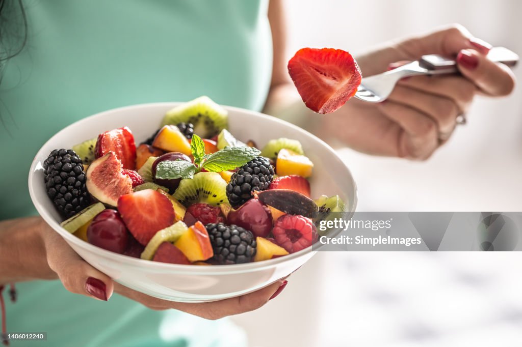 A woman breakfasts a fruit salad high in vitamins and fiber.