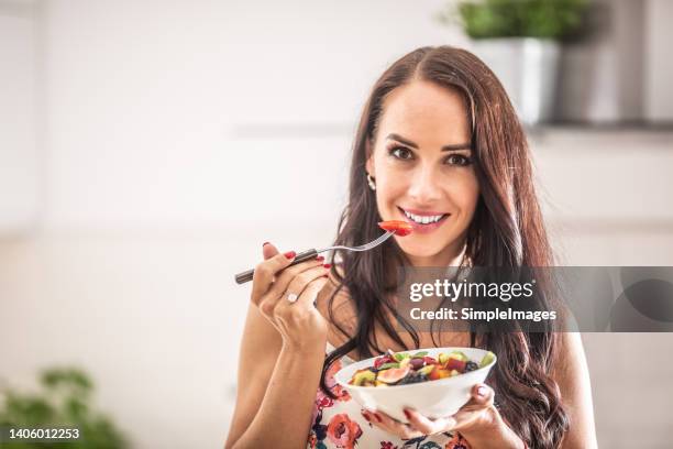 young woman eating healthy fruit salad in her kitchen. - kiwi foto e immagini stock