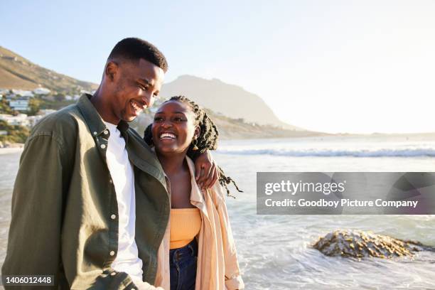 smiling young couple walking together along a beach in summer - young couple on beach stock pictures, royalty-free photos & images