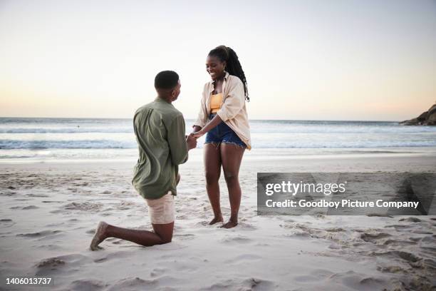 joven proponiéndole matrimonio a su novia en una playa de arena al atardecer - prometido relación humana fotografías e imágenes de stock