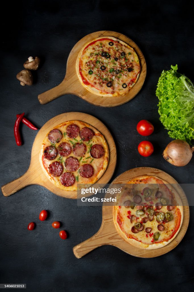 Pizza party dinner. Flat-lay of various kinds of Italian pizza over rustic wooden table, top view, wide composition. Fast food lunch, celebration, gathering concept.