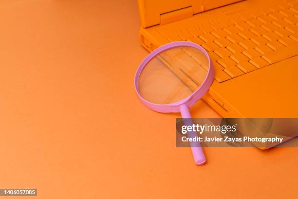 orange laptop and pink magnifying glass on orange background - spotting stock pictures, royalty-free photos & images