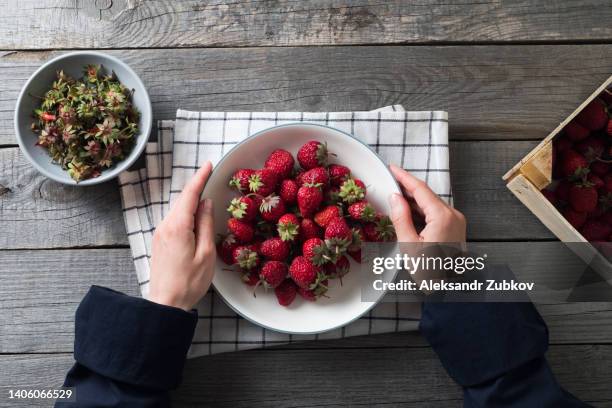 red ripe strawberries in a bowl or ceramic plate on a wooden background or table. a woman or a girl has a large berry in her hands, she eats it. the concept of vegetarian, vegan and raw food nutrition and diet. from the farm to the table. vegetable food. - big country breakfast stock-fotos und bilder