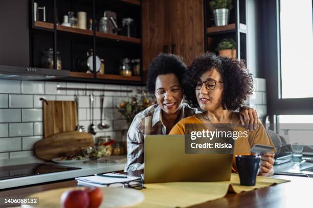 two mature women buying online at home - mid adult couple stock pictures, royalty-free photos & images