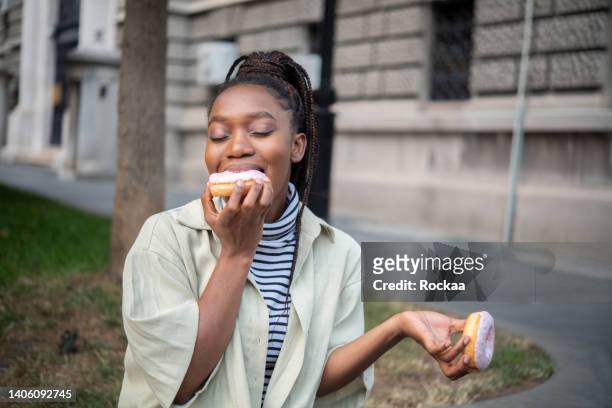positive young african woman - eating donuts stockfoto's en -beelden