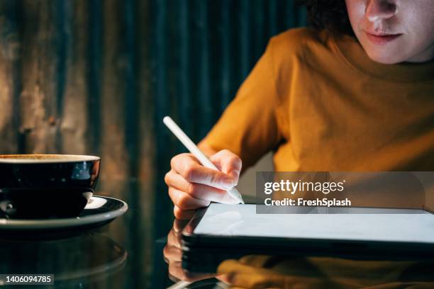 anonymous woman dressed in a yellow ocher t-shirt drawing on her digital tablet while having a cup of coffee - yellow dress stock pictures, royalty-free photos & images