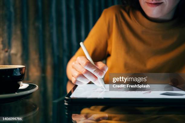 anonymous woman dressed in a yellow ocher t-shirt drawing on her digital tablet while having a cup of coffee - tablet close up real copyspace stock pictures, royalty-free photos & images