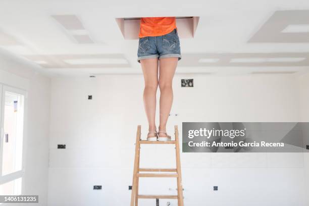 woman climbs stairs and peeks through attic hatch during home renovations - attic stock pictures, royalty-free photos & images