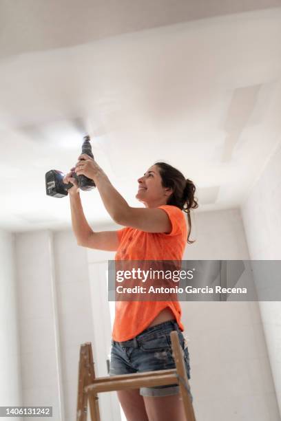 woman drilling the ceiling during home renovations - broca imagens e fotografias de stock
