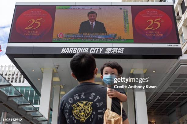 Man holding a child walks in front of a screen showing a live broadcast of Chinese President Xi Jinping speaking during a swearing-in ceremony for...