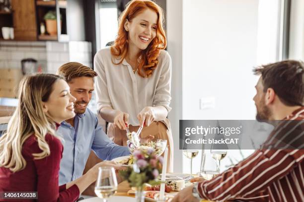 beautiful woman serving salad to friends during dinner party at home - party host imagens e fotografias de stock